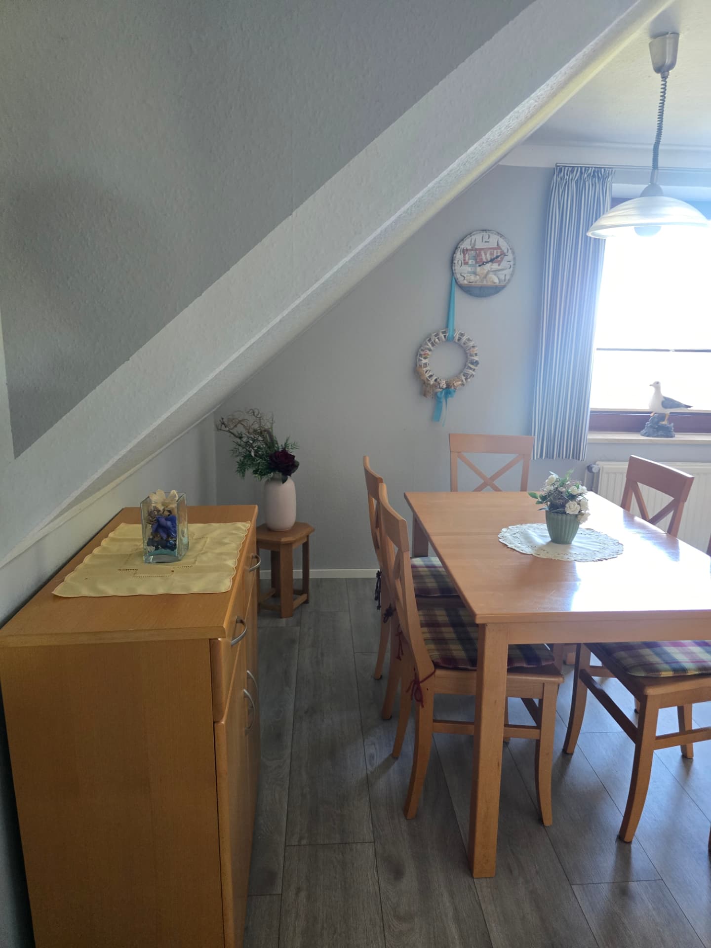 Essbereich mit Holztisch, Wanduhr und Muschelkranz in der Muscheln Wohnung