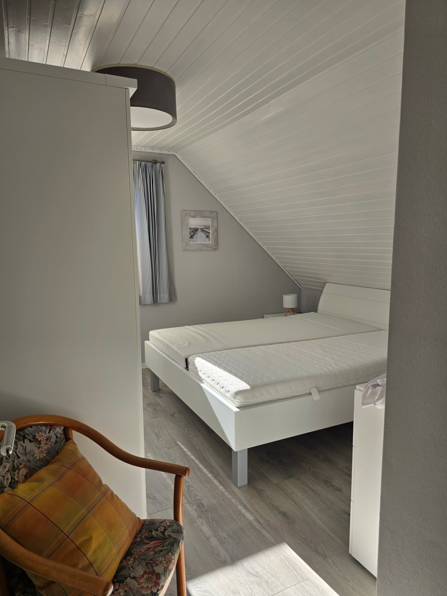 Schlafzimmer mit weißem Doppelbett, Kommode und Sessel unter der Dachschräge