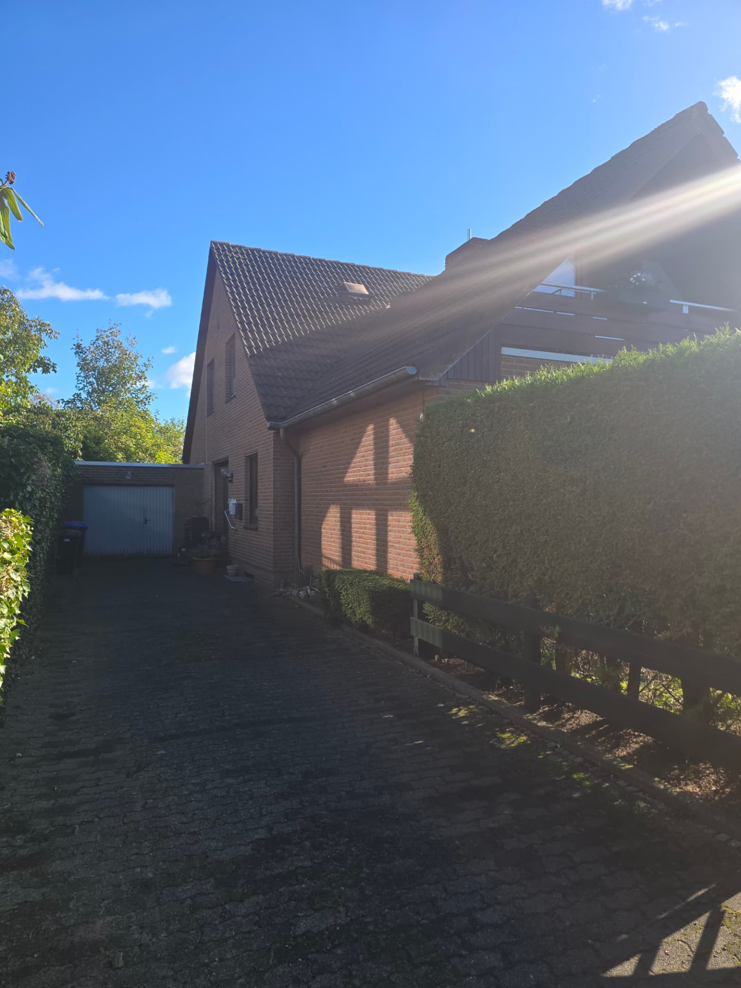 Backsteinhaus mit gepflasterter Zufahrt, Garage, Hecke und Holzzaun
